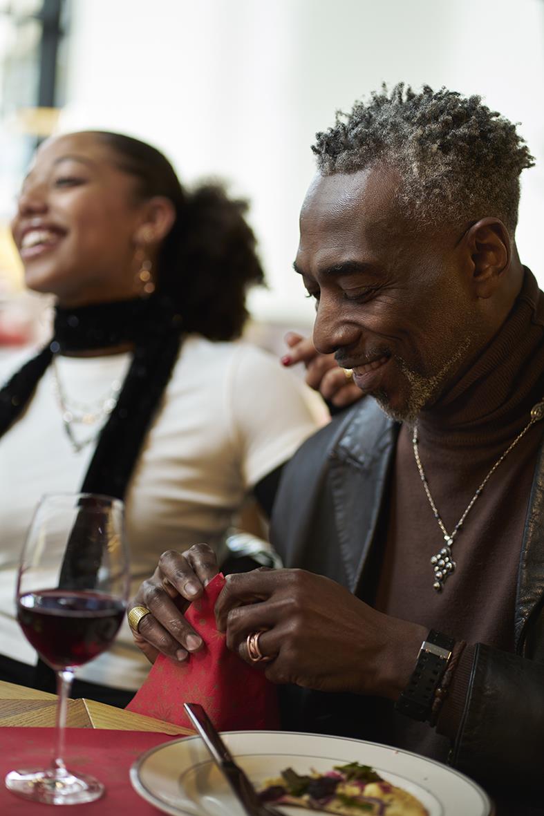 Två personer som äter och dricker vin vid ett bord, glad stämning, kvinna i vit topp och man i mörk jacka