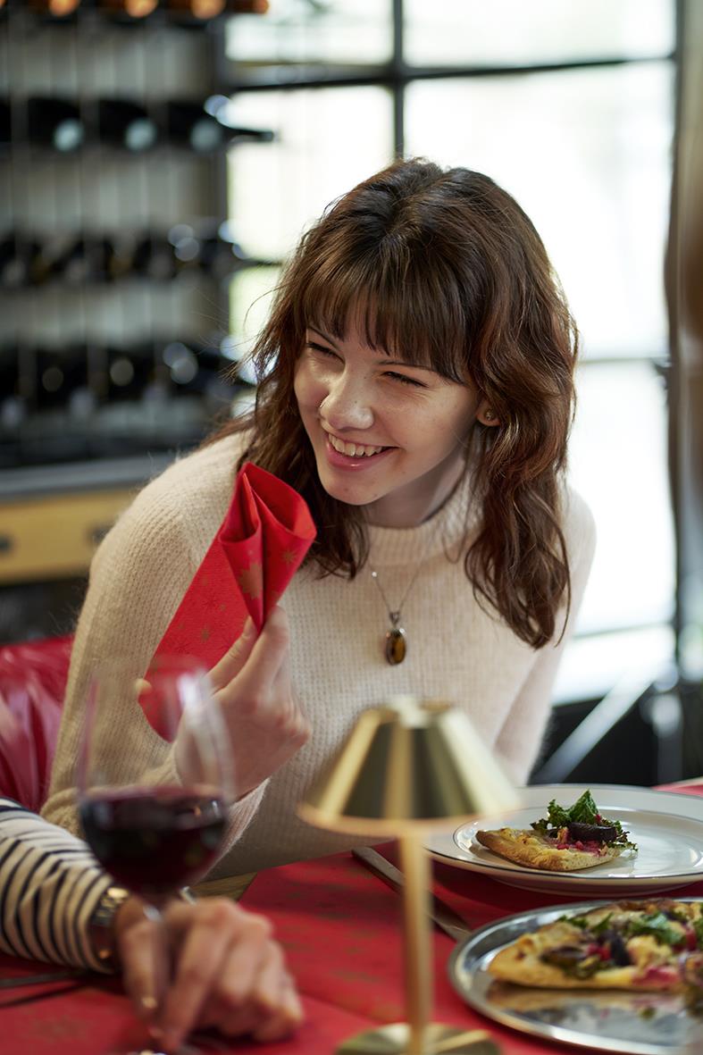 Kvinna ler och håller en röd servett, middagsbord med vin och mat i ett mysigt kök