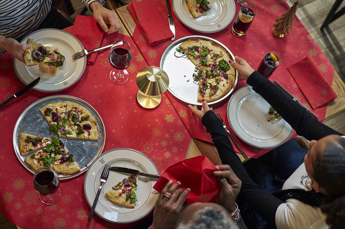 Dukning av bord med pizza, vin och juldekorationer, person som placerar en tallrik