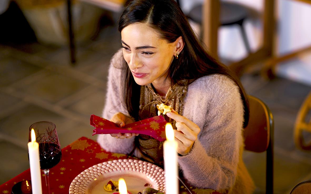 Kvinna som äter vid ett bord med röd duk och ljuslyktor, stämningsfull inomhusmiljö