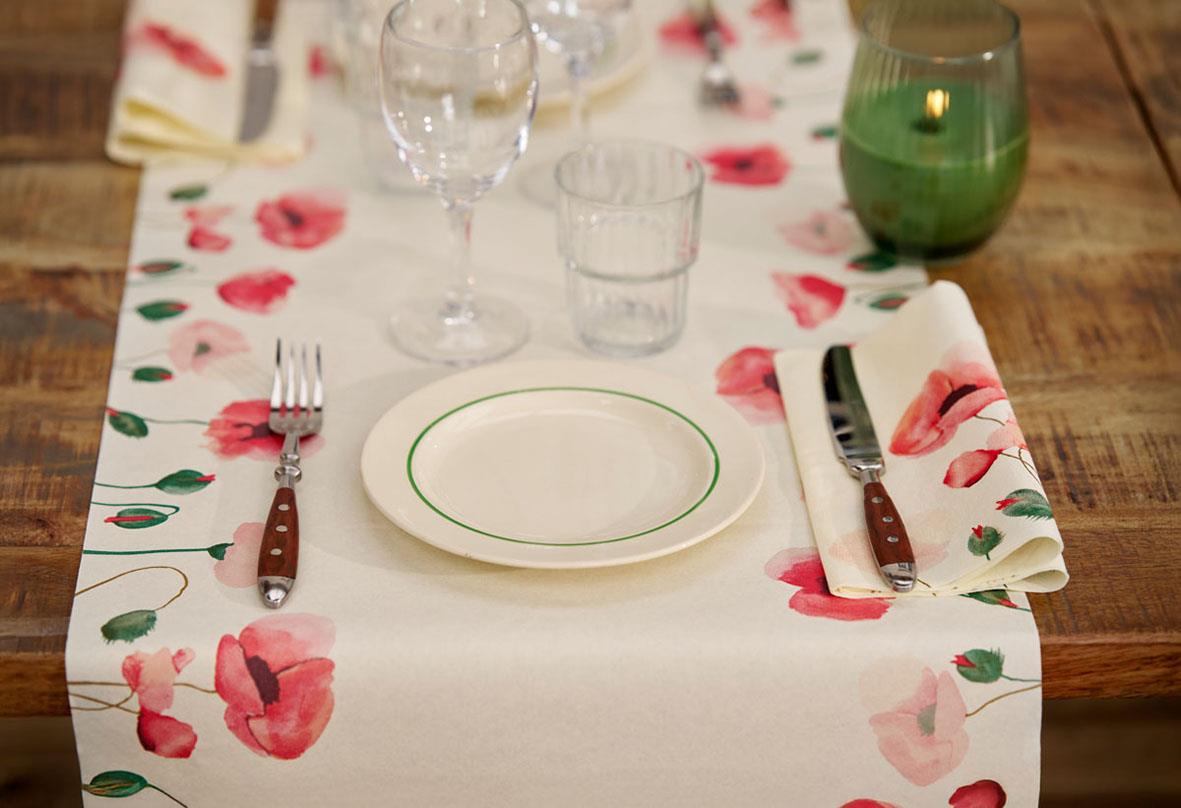 Borddukning med blommönstrad duk, tallrik, glas, bestick och servett på träbord