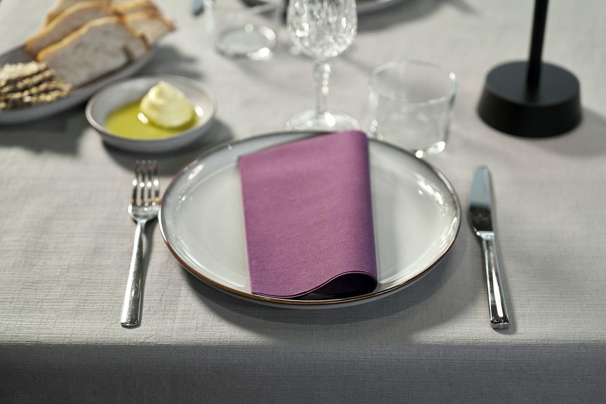 Borddukning med vit tallrik, lila servett, bestick och glas på dukad bord