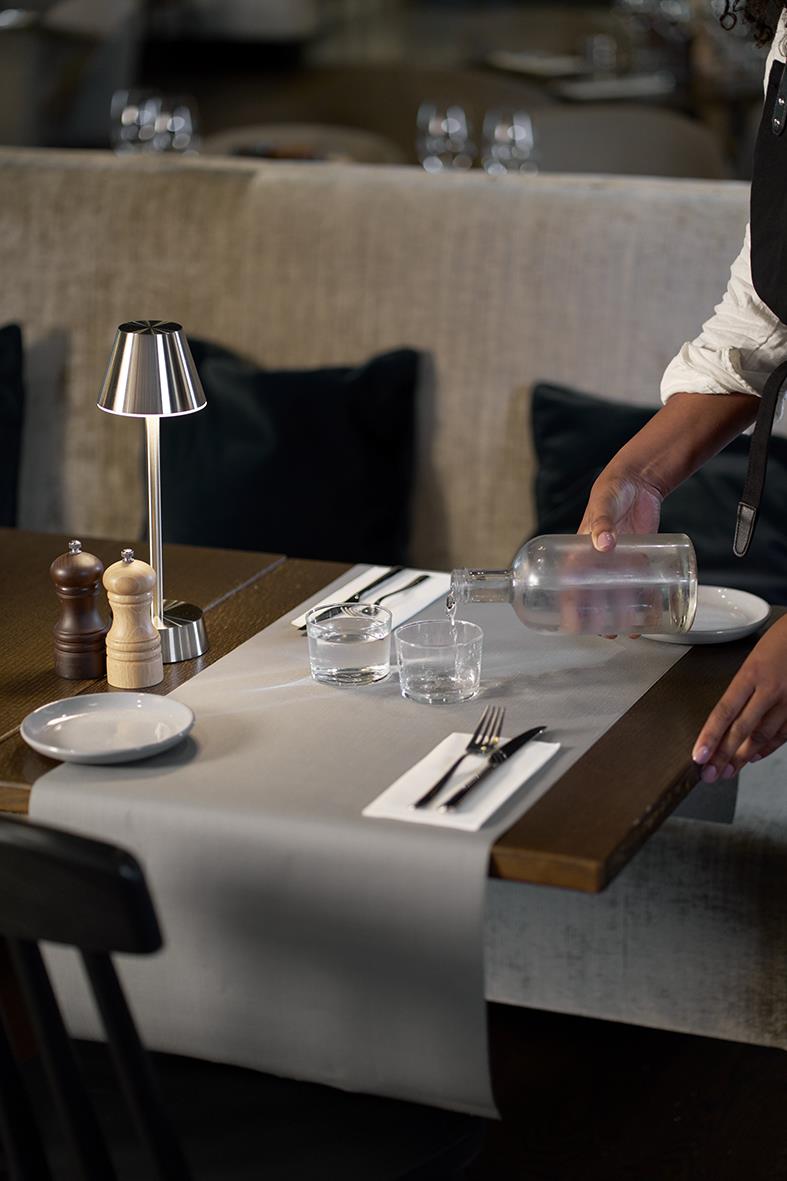Bord med vit löpare, salt- och peppar, vatten och bestick, person häller vatten på restaurang