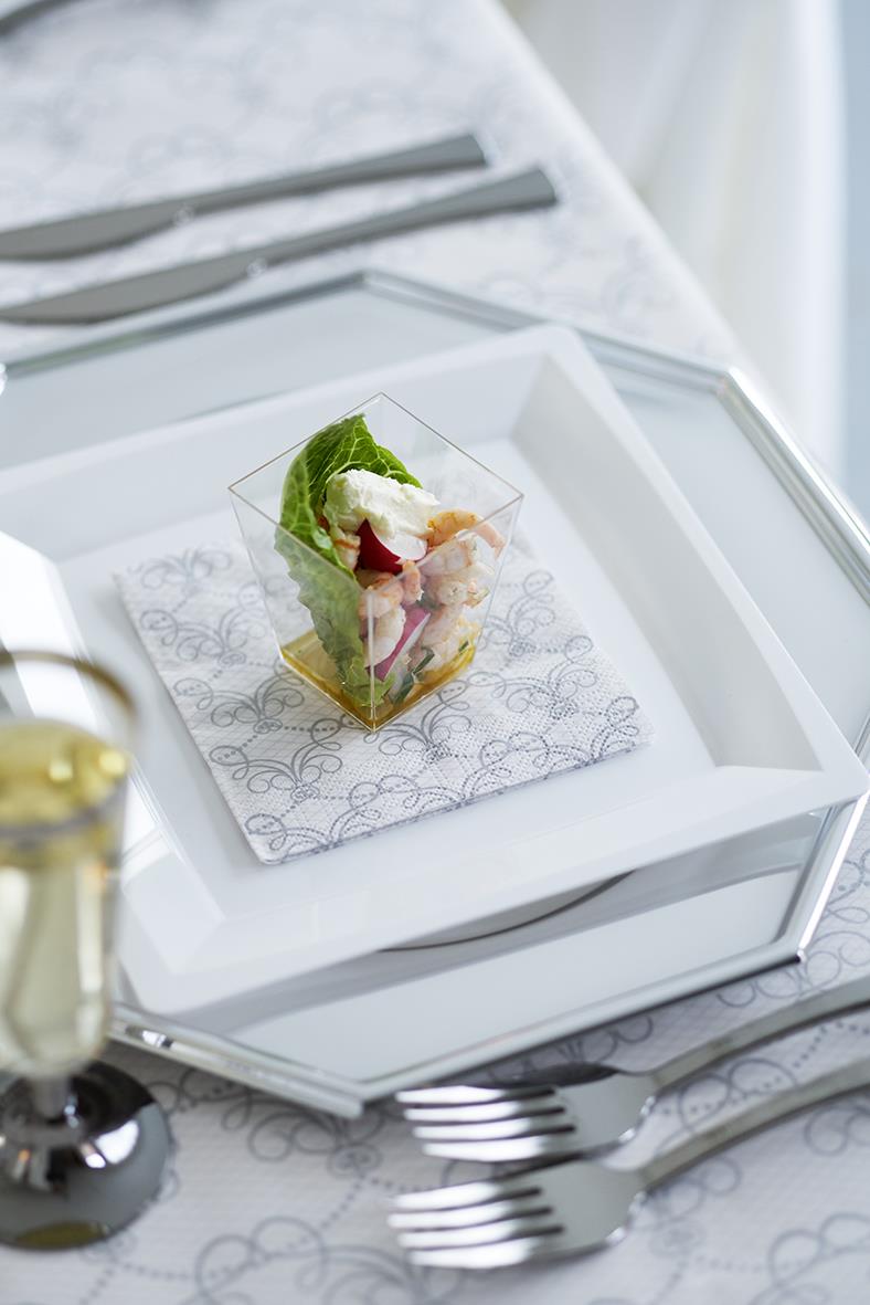 Fyrkantig transparent plastbägare med sallad på ett vitt serveringsfat