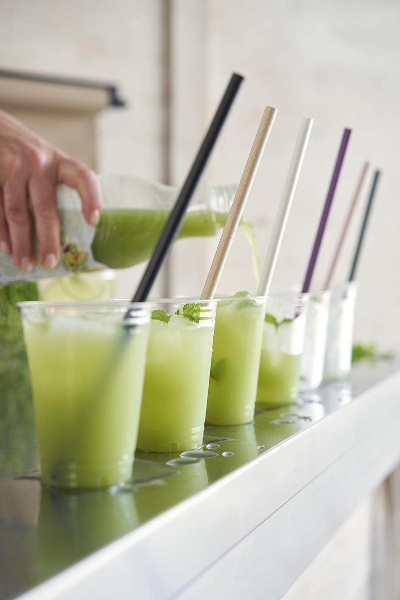 Flera gröna drycker i klara glas med svarta, vita och lila sugrör på ett vitt bord