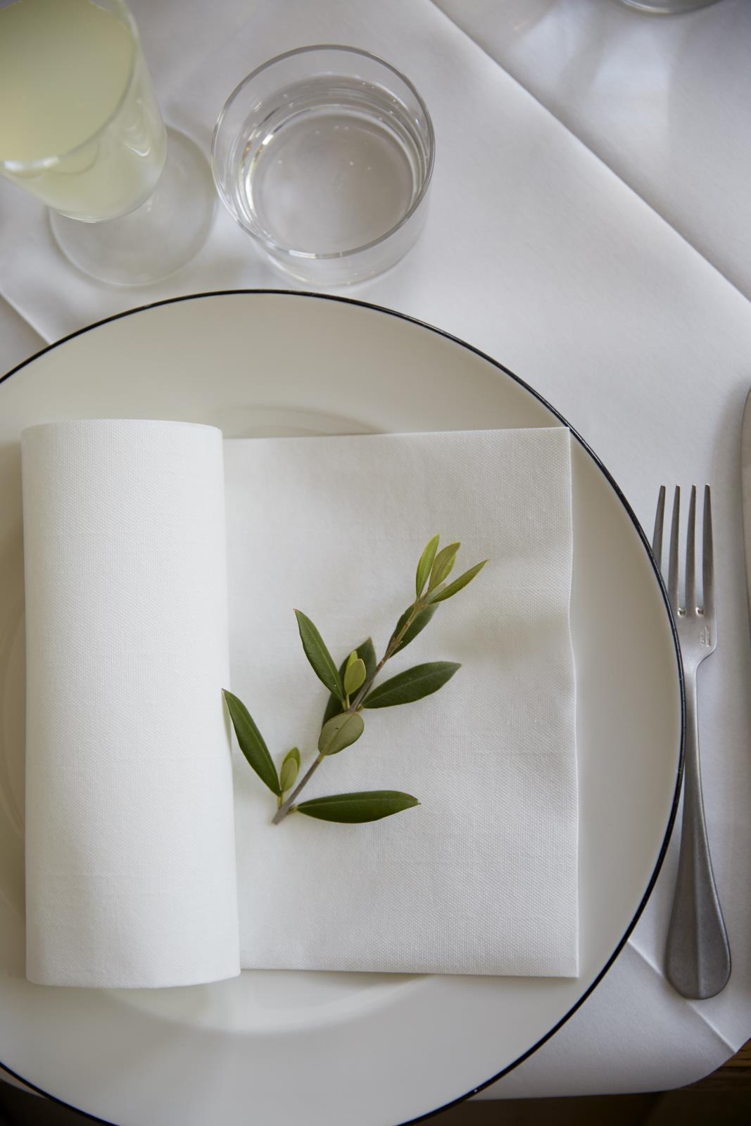 Vit servett Duni Dunilin 40x40cm med grön kvist på tallrik med bestick och drycker