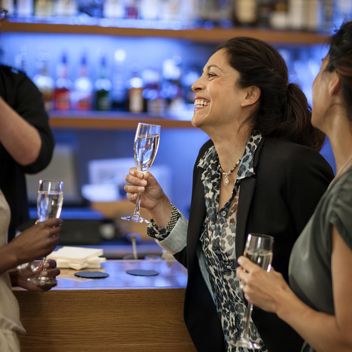 Kvinna som skrattar och håller ett glas champagne i en bar eller restaurangmiljö
