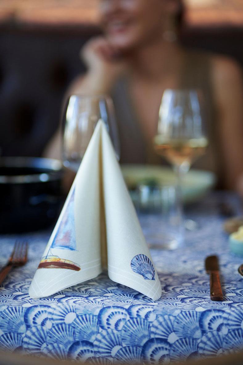 Servett Duni Dunisoft Tide Beige 40x40cm vikta på ett bord med glas och bestick i bakgrunden