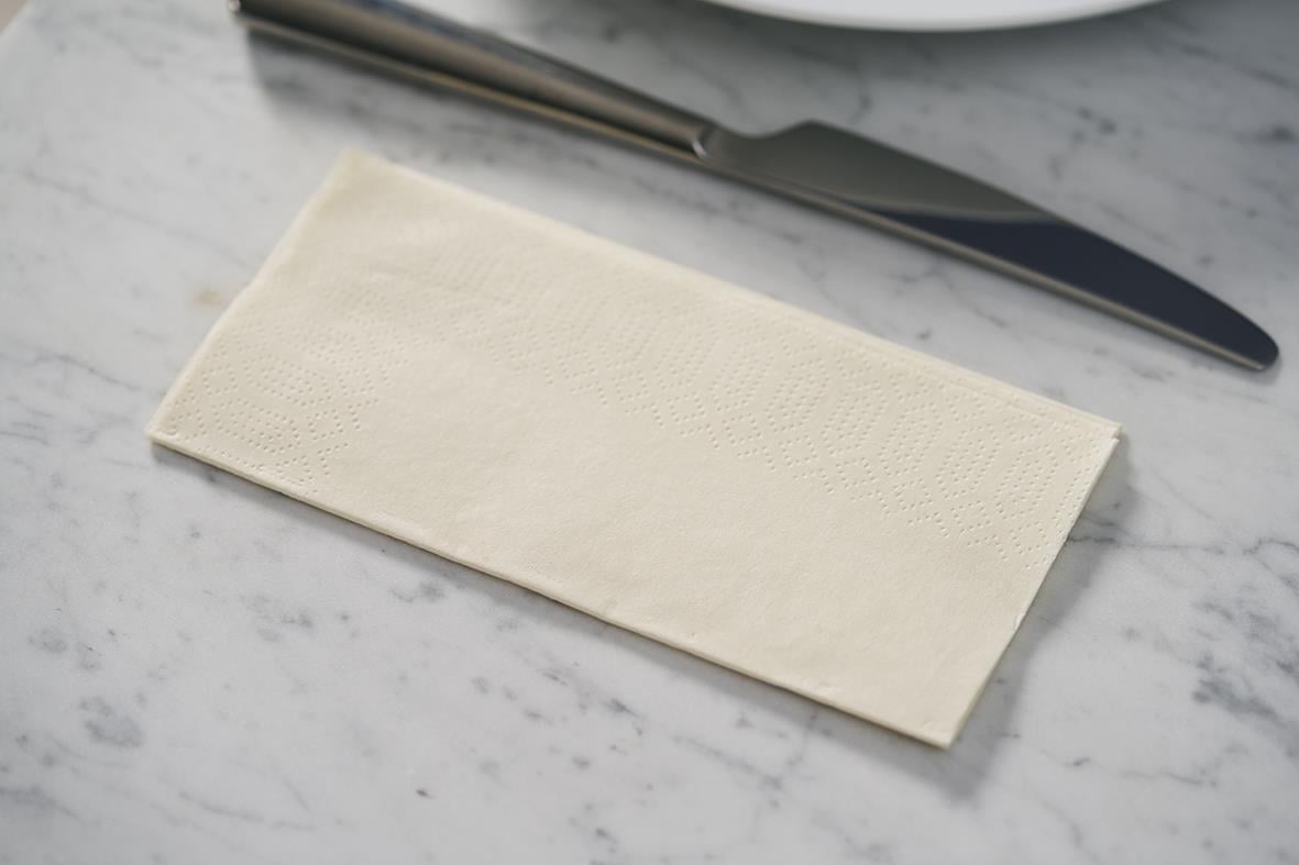 En vit servett Duni 3-lag 1/8 Vikt Cream 33x33cm på en marmorbord