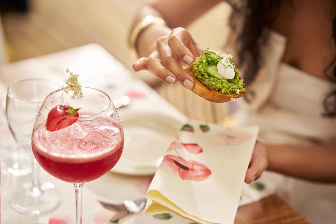 Person som serverar en liten smörgås med grönt på en dukad bordsscen