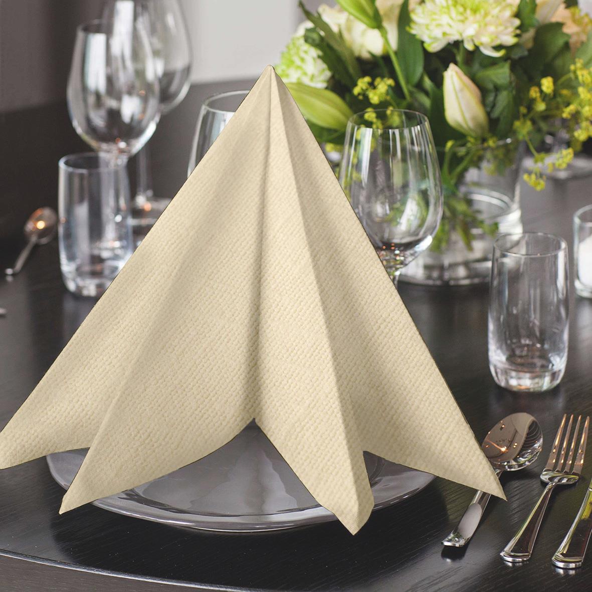 Servett Tork LinStyle 1/4 Vikt Creme 39x39cm i beige färg, vikta på duk med glas, bestick och blomsterarrangemang i bakgrunden