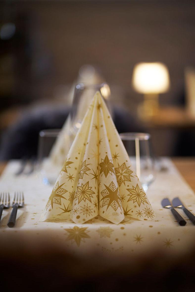 Servett i vitt och guld med julstjärnor och snöflingor, vikt till en elegant juldukning på ett bord