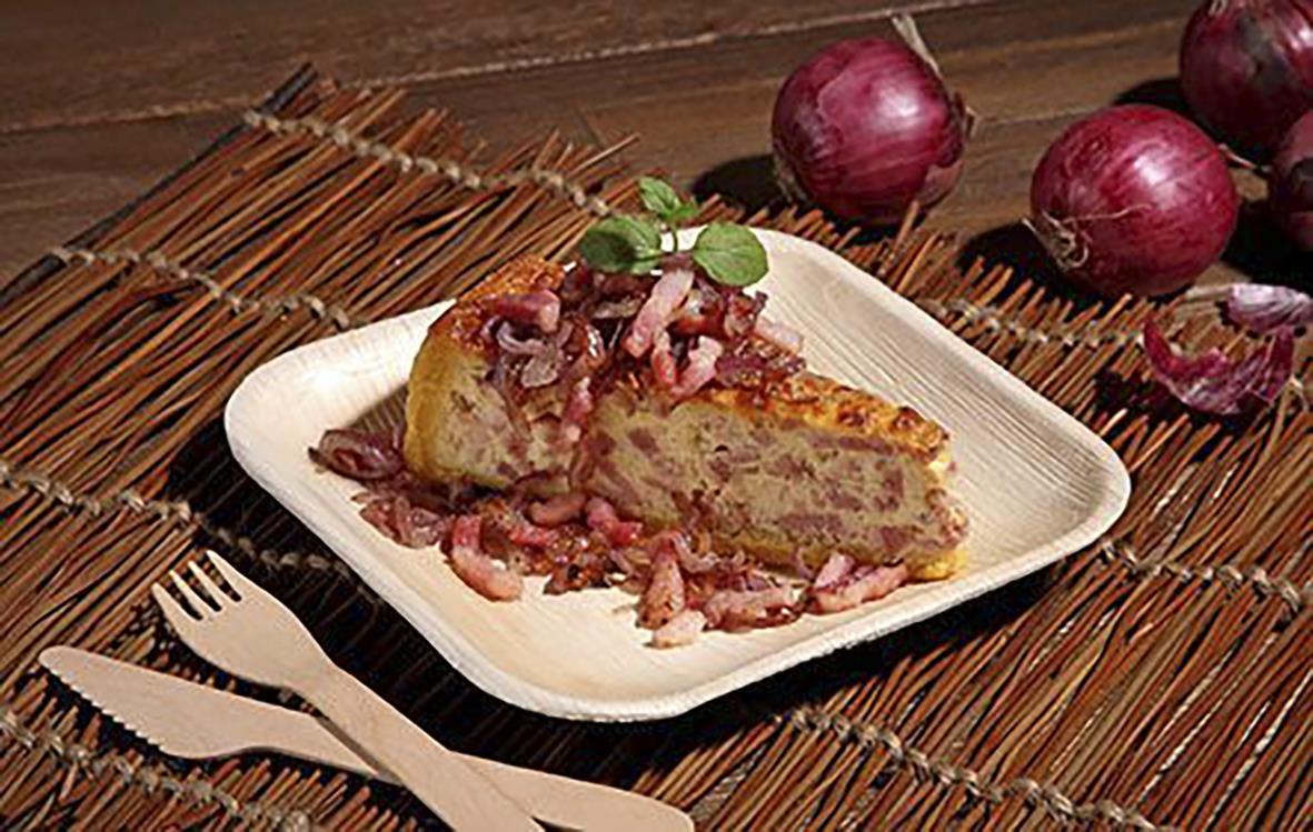 Engångstallrik av palmblad med bit av paj och lök i bakgrunden