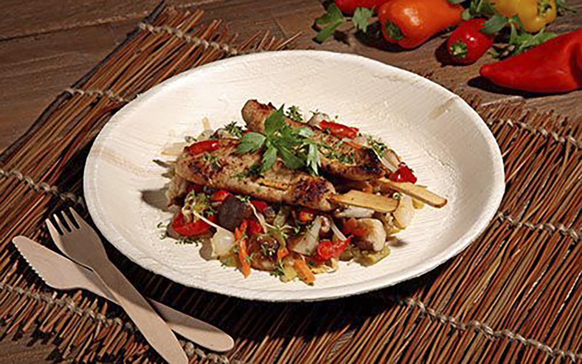 Engångstallrik av palmblad, rund, 23 cm, med mat och garnering på en träunderlag