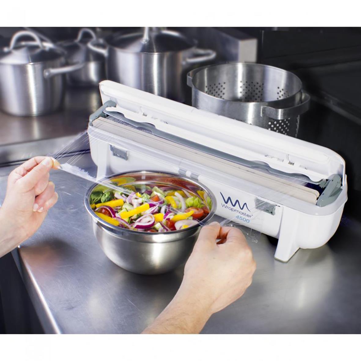 Dispenser Wrapmaster 4500 45cm i kök, används för att skära och förpacka matvaror, med en person som använder den för att förpacka en sallad.