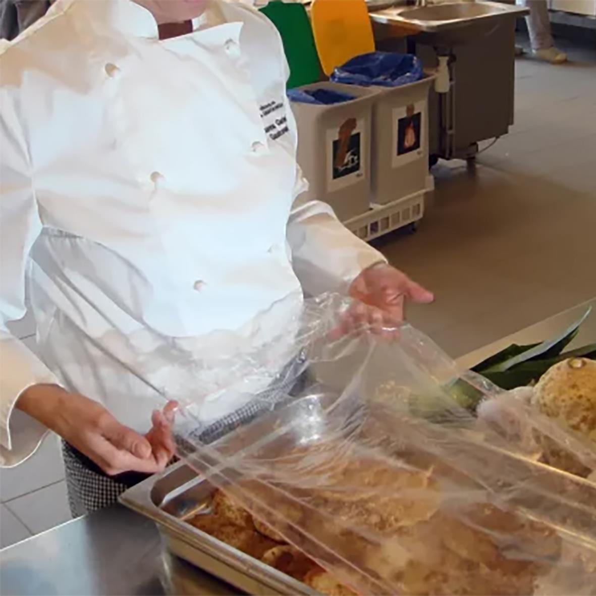 Person som placerar ett plastöverdrag på en matlåda i ett kök