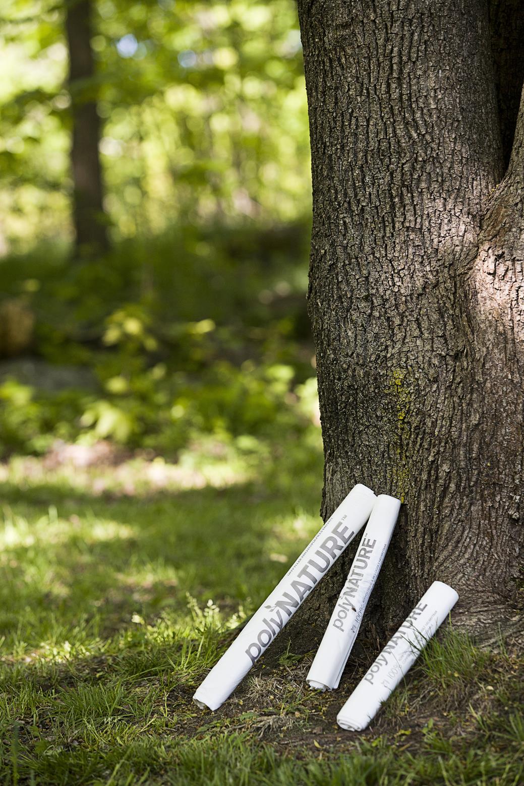 Två vita sopsäckar med texten Poly Nature lutade mot ett träd i en skog