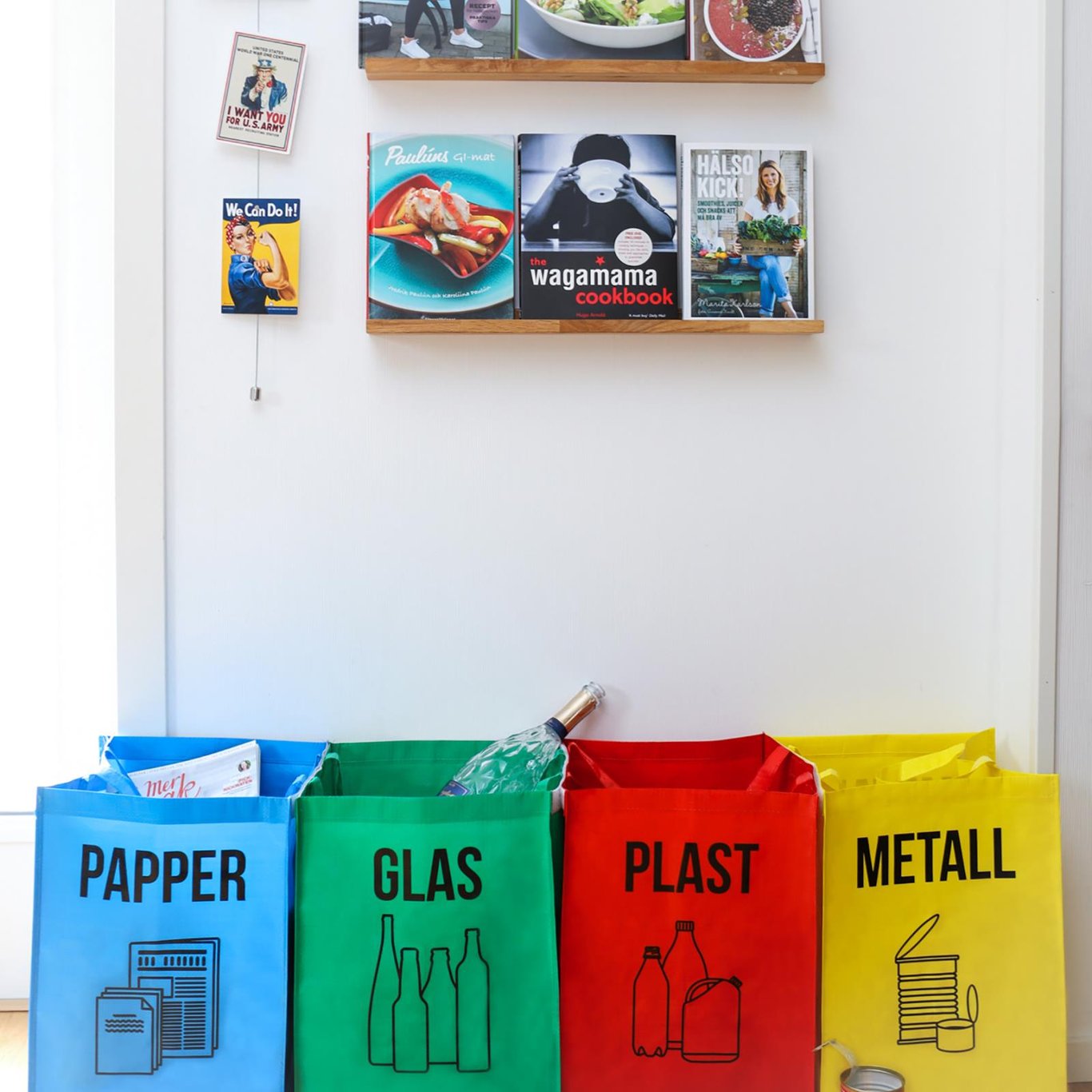 Källsorteringsset med plast, glas, papper och metallpåsar framför en vägg med böcker och affischer