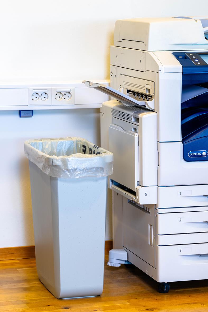 Sopsäck i plast i en papperskorg bredvid en kopieringsmaskin på ett kontor