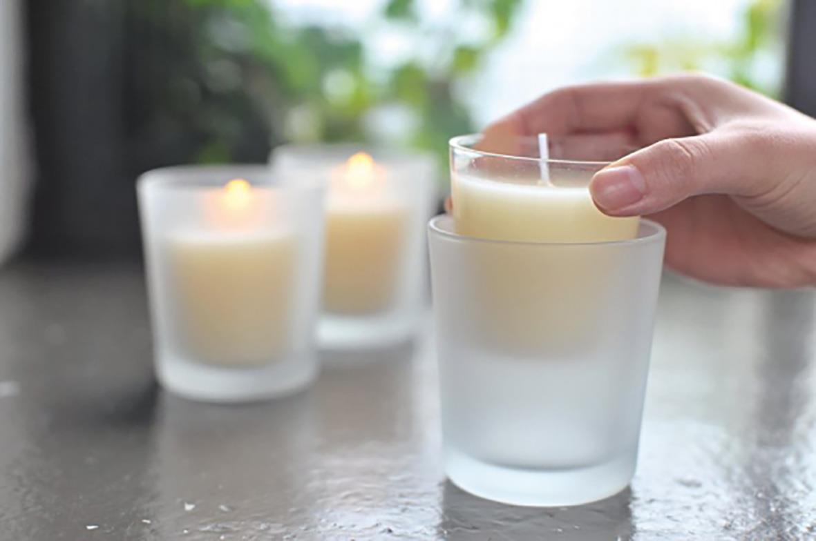 Hand placerar ett vitt Duni Switch & Shine ljus i ett frostat glas, tre liknande ljus i bakgrunden