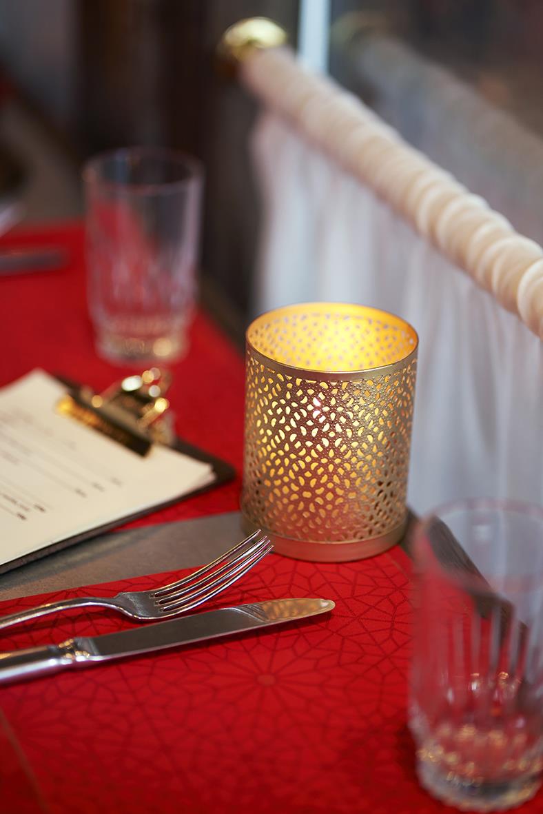 Guldfärgad ljushållare Duni Bliss med perforerad design på ett bord med röd duk och glas