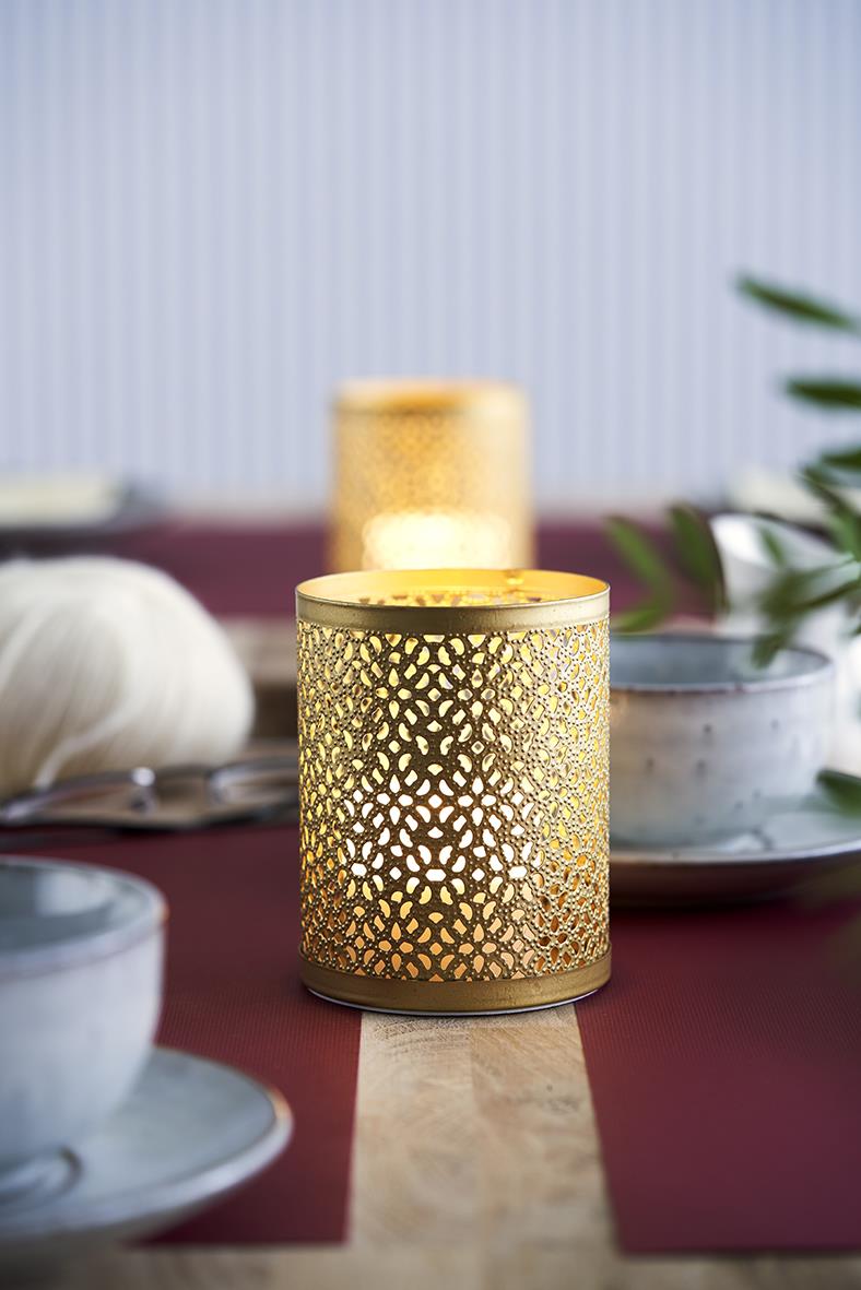 Guldig ljushållare Duni Bliss med dekorativ perforerad design på bord med tallrikar och gröna blad