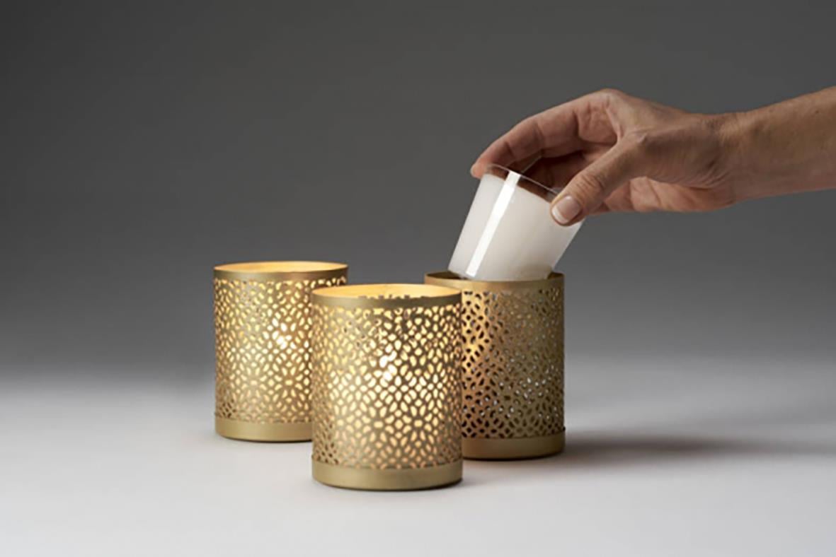 Hand placerar ett ljus i en guldljushållare Duni Bliss Guld 100x80mm