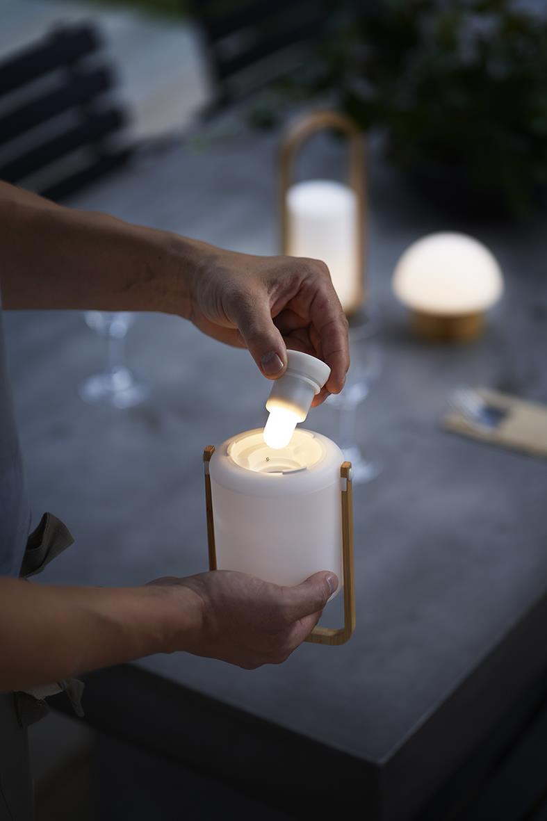 Person placerar LED-ljushållare Duni Easy Bambu på ett bord, omgivning med andra ljus och bord