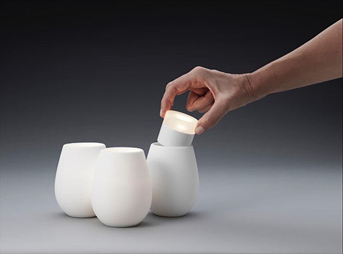 Vit silikon ljushållare Duni för LED-ljus, 103xØ85mm, tre stycken, en hand placerar ett ljus i en av hållarna