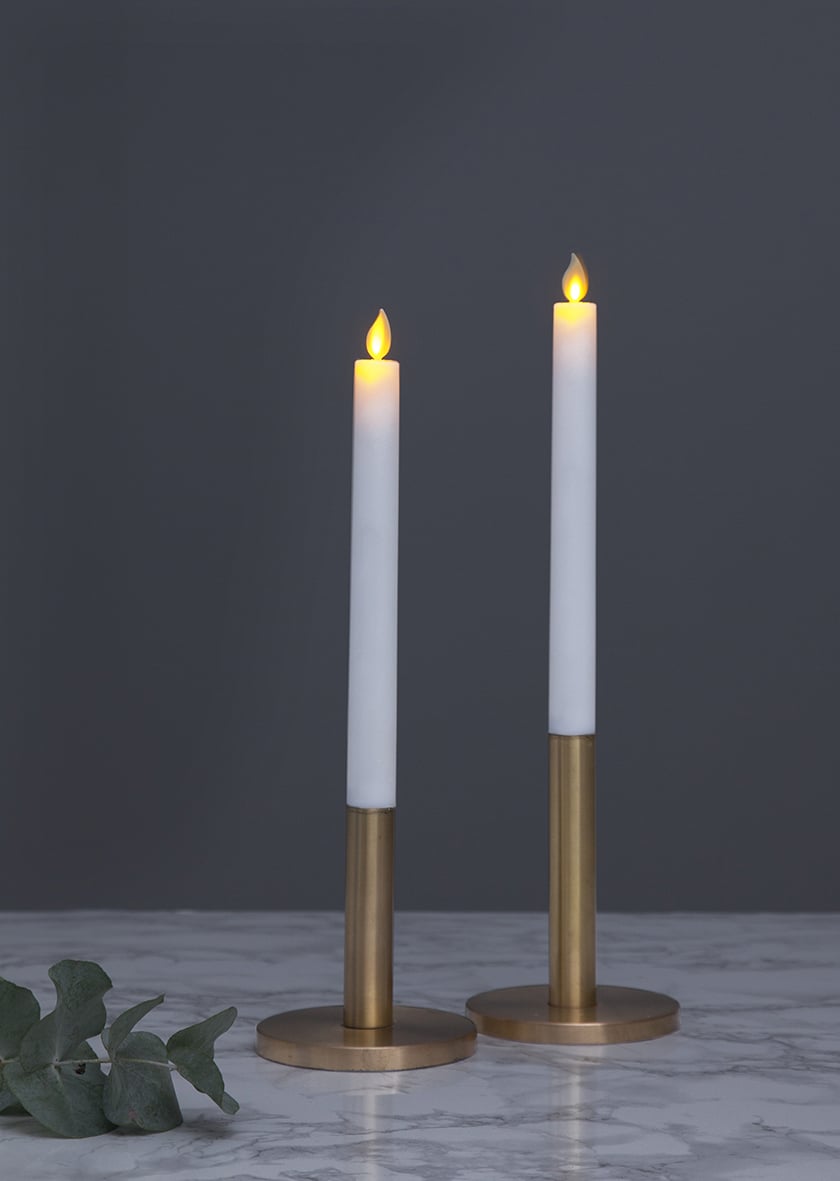 Två LED-ljus i antikstil med brinnande låga, guldfärgade stakar på en marmorbord