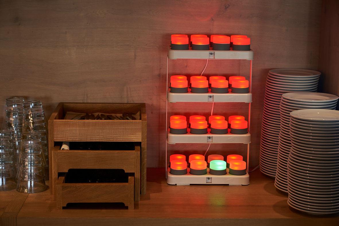 LED Duni laddningsstation i vitt med orange och gröna lampor, omgiven av tallrikar och glas