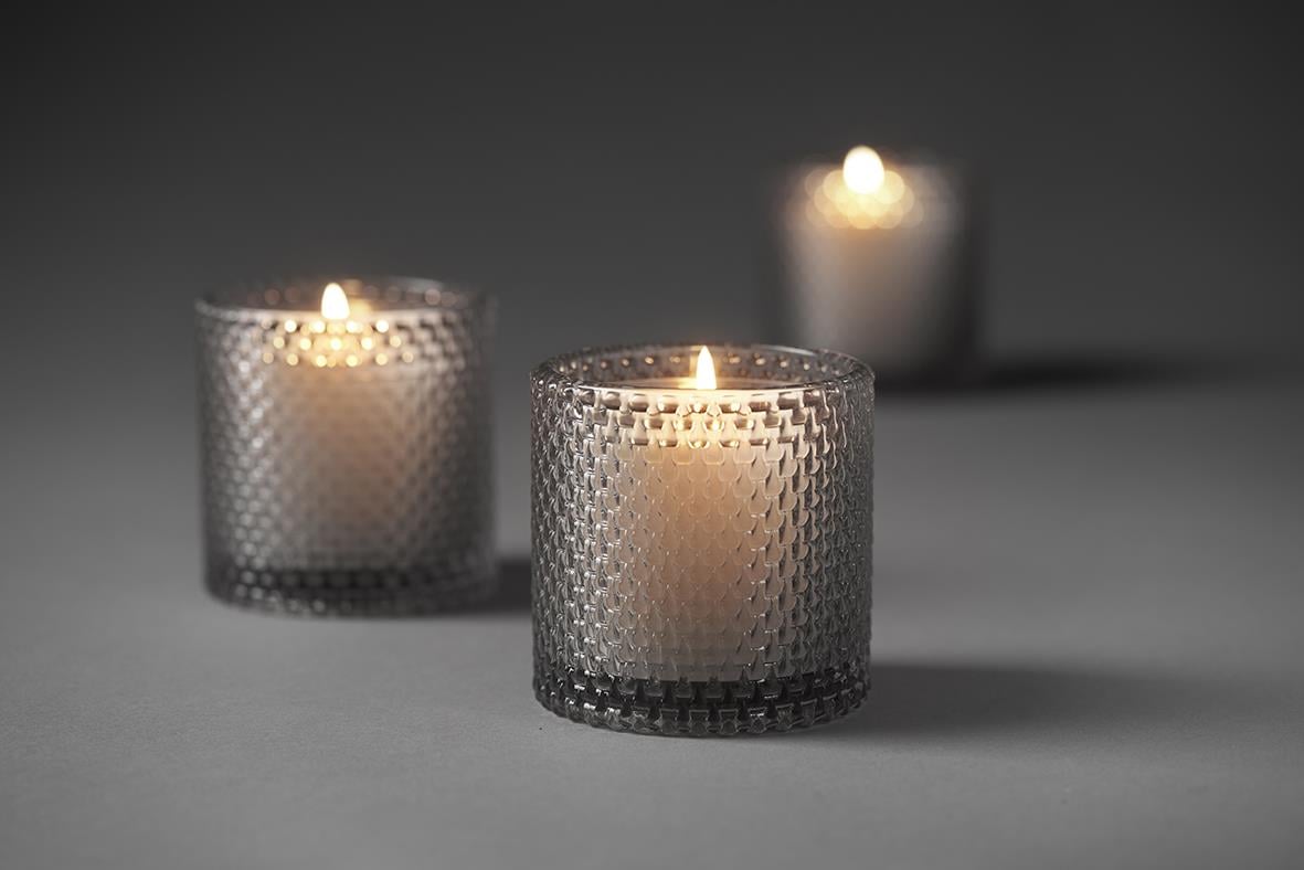 Tre ljuslyktor i glas med dimmigt mönster, tända ljus inuti, på mörk bakgrund