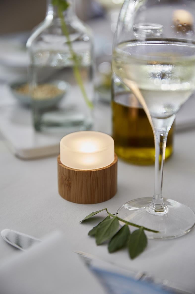 Liten LED-ljushållare i bambu på bord med glas och växter, mysig belysning