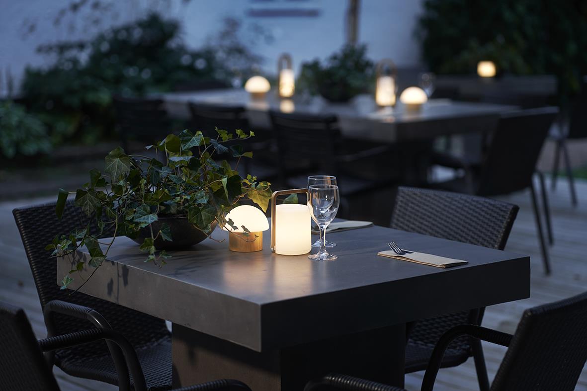 Uteplats med ljushållare LED Duni Brother Bambu på bordet, omgivning med stolar och tända ljus i skymningen