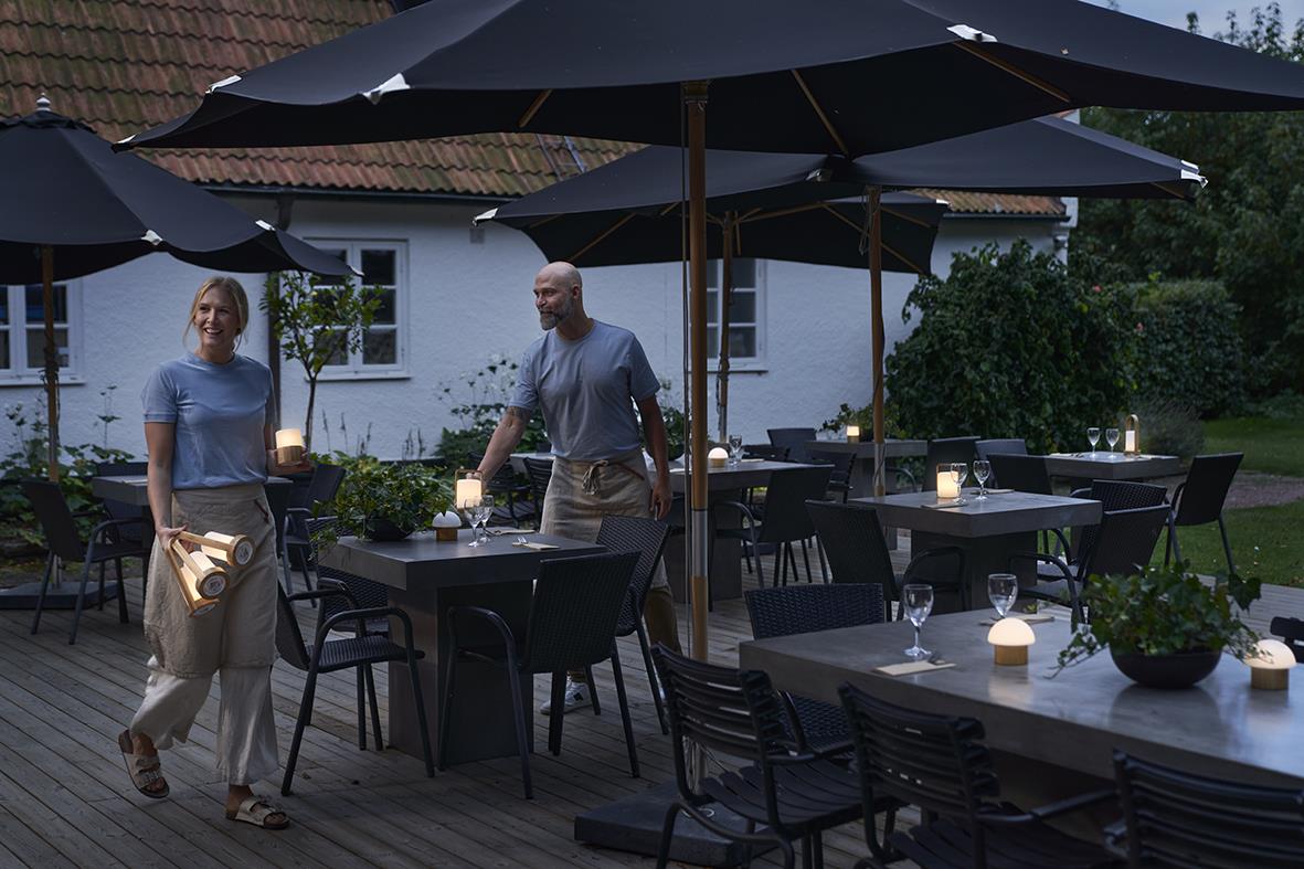 Uteplats med bord, stolar och LED-ljushållare under parasoller på kvällen