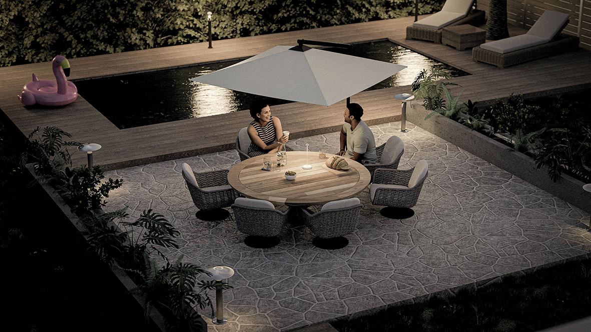 Tre personer sitter runt ett runt bord med en stor vit parasoll utomhus vid en pool på kvällen