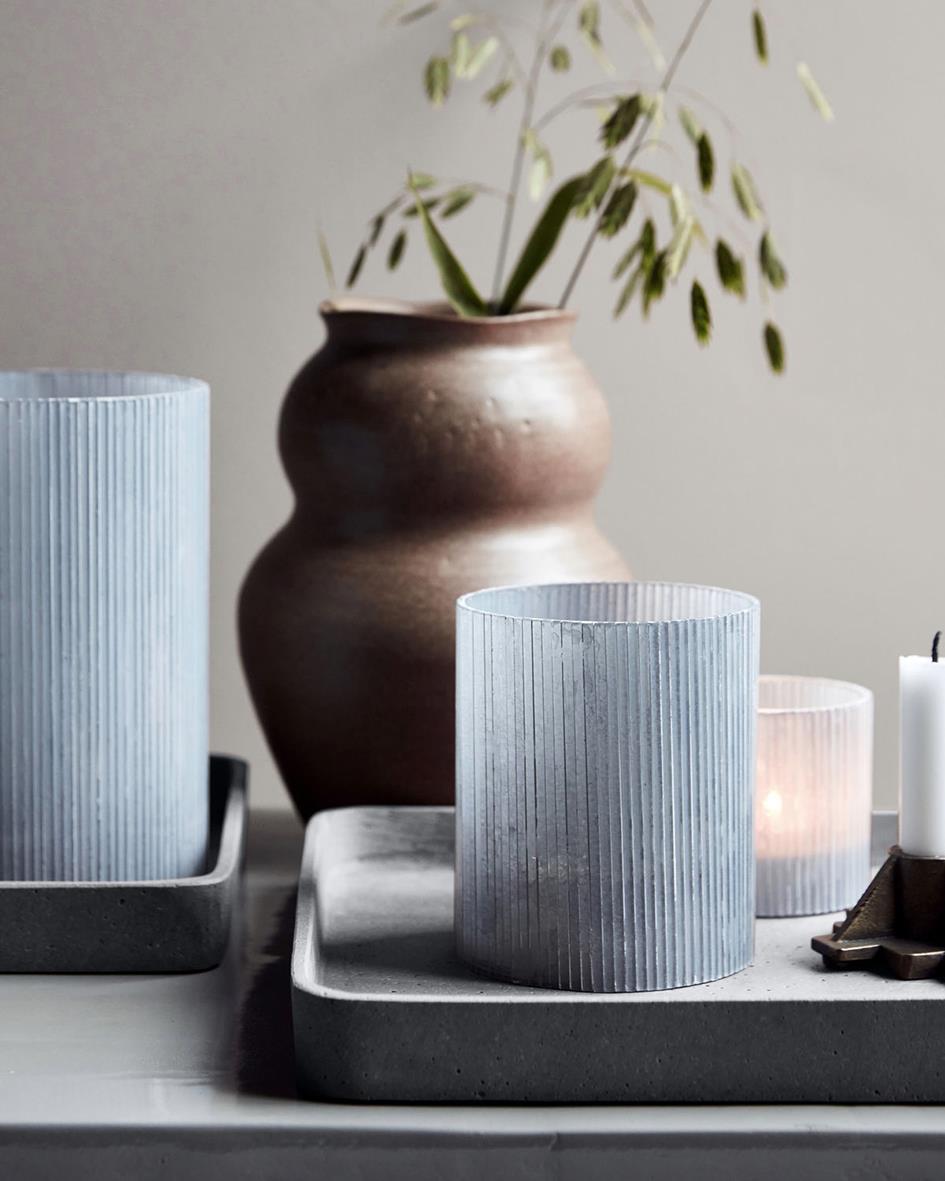 Ljushållare House Doctor Mirr Frostgrå Ø10x12,5cm med ljus på en bricka och en vas med växt i bakgrunden