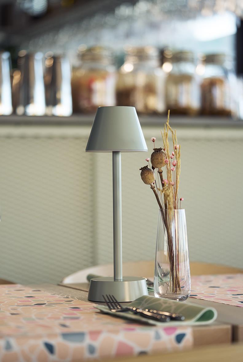 Bordslampa LED Duni Zelda i ljusgrön på ett bord med bestick och en vas med torkade blommor