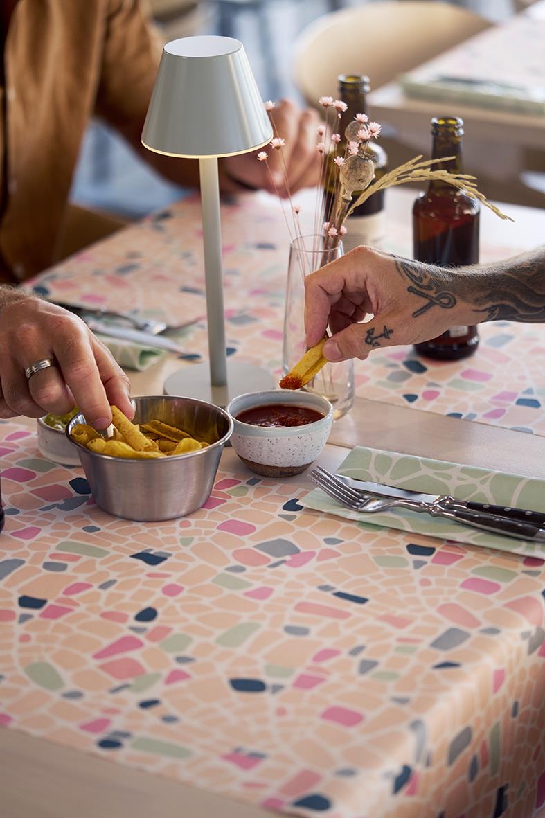 Bord med bordslampa LED Duni Zelda i ljusgrön, mat och dryck, hand som doppar pommes i sås, blommor i glas, person med tatuering