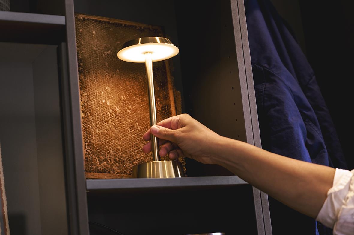 Hand som placerar en mässingsfärgad LED-bordslampa på en hylla