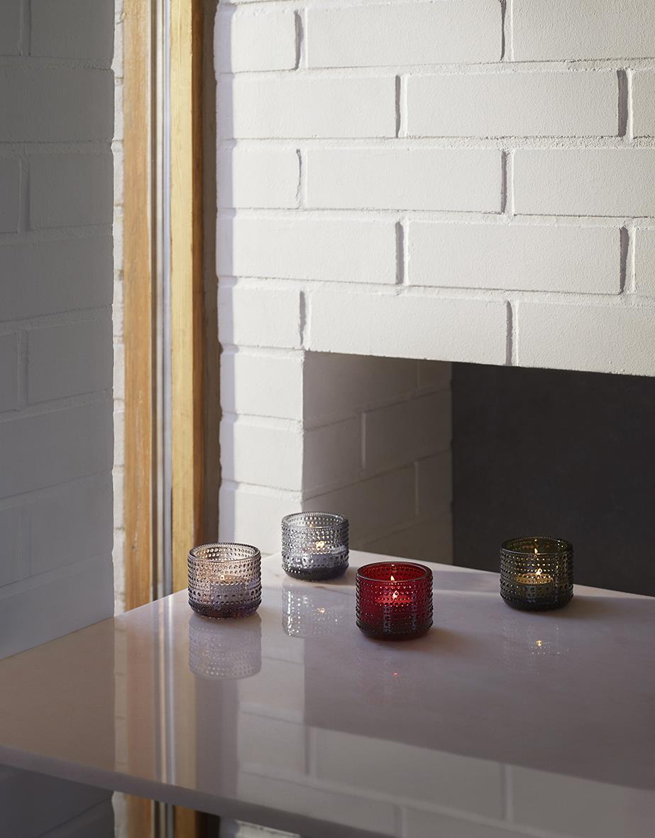 Fyra små ljuslyktor i olika färger och mönster på ett vitt bord framför en vit tegelvägg och en öppen spis