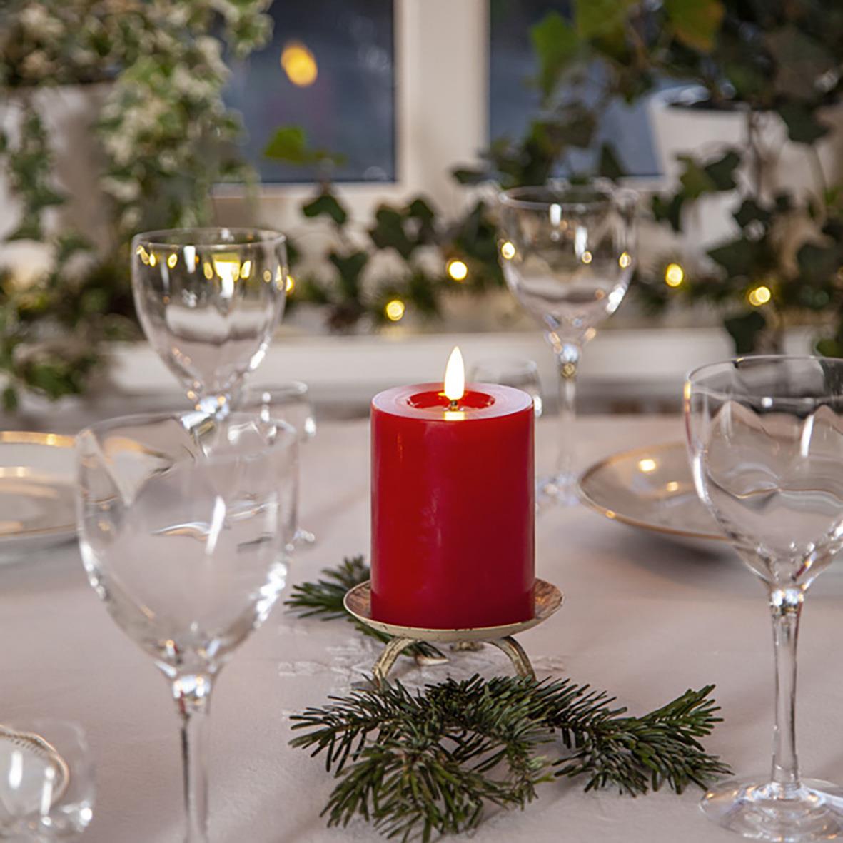 Röd LED blockljus med flammande effekt på julbord, omringad av glas och granris