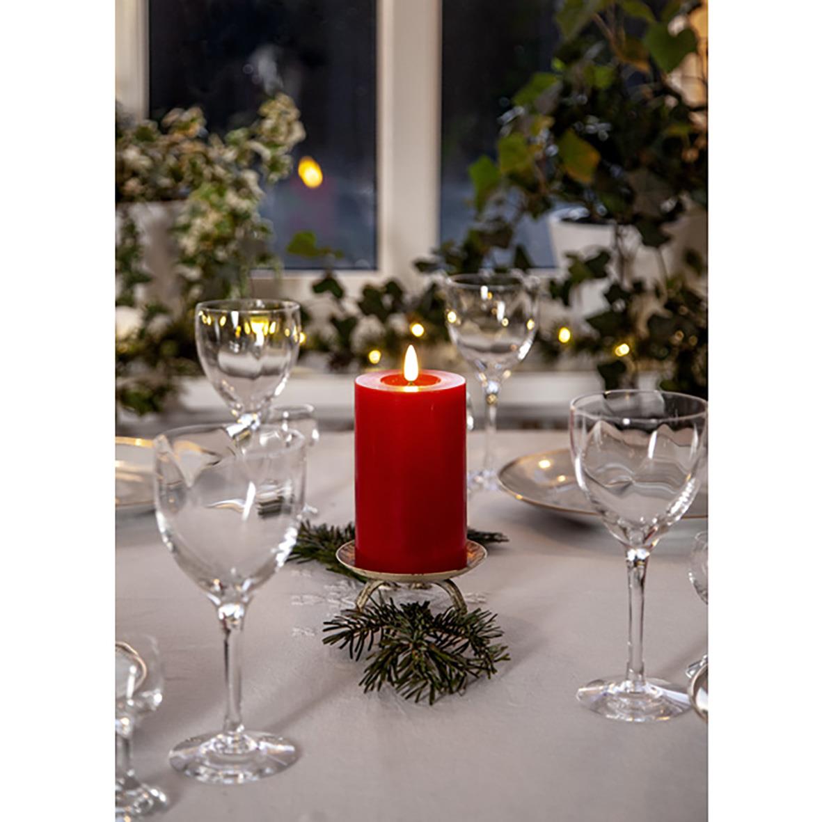 Röd LED-blockljus med flammaeffekt på ett bord med glas och juldekorationer
