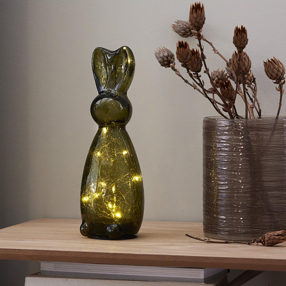 Grön glasdekoration i form av en kaninfigur bredvid en vas med torkade blommor