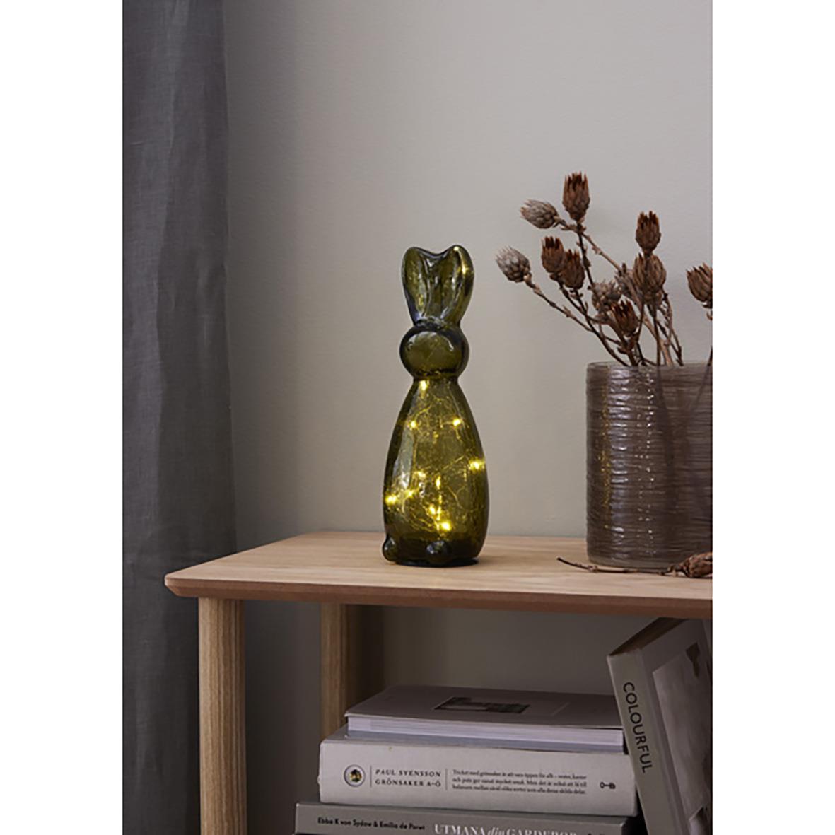 Glasdekoration i form av en katt på ett bord bredvid en vas med torkade blommor