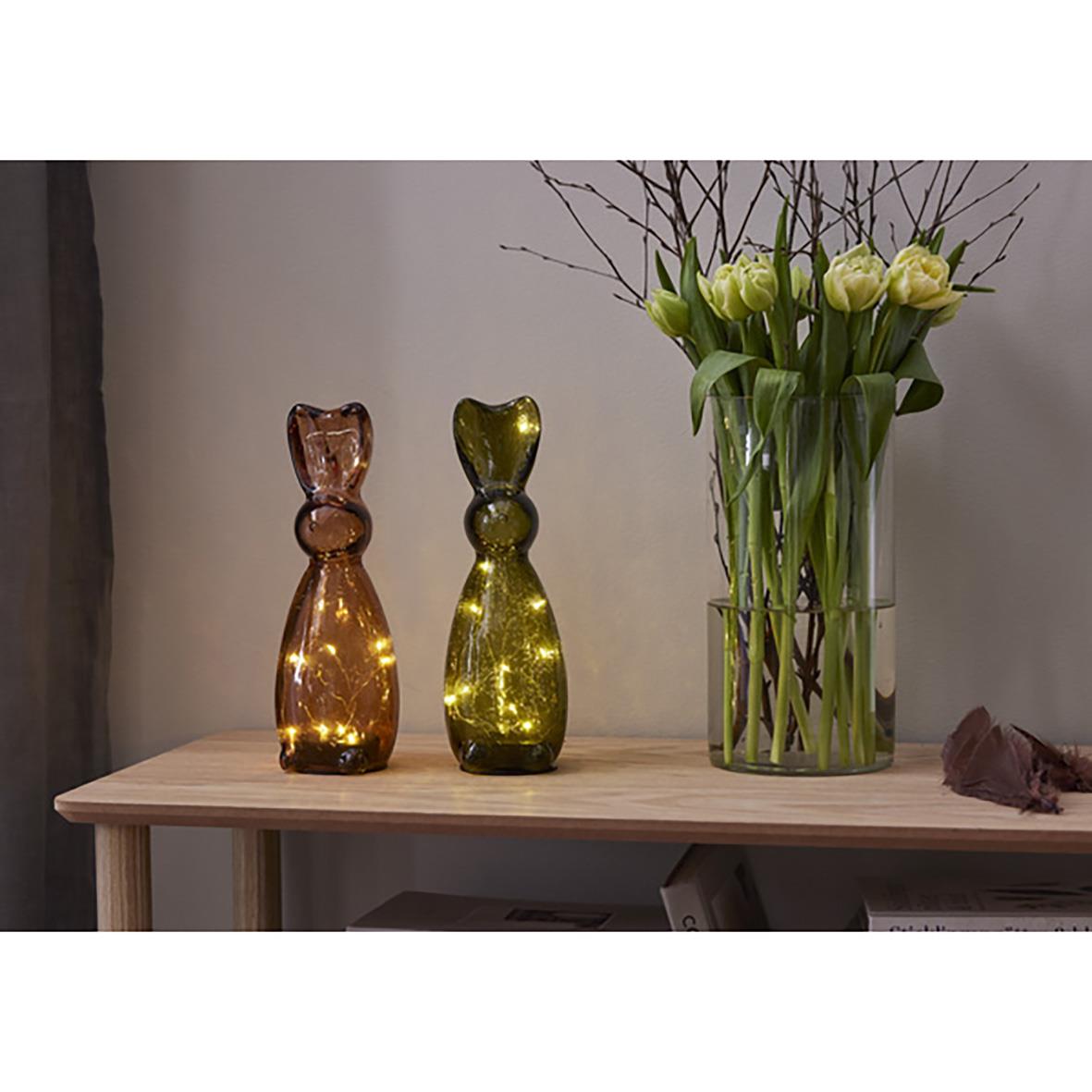 Två glaskatter i brunt och grönt samt en vas med gula tulpaner på ett träbord