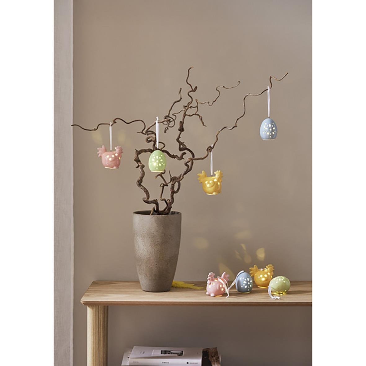 Dekorationsfigurer Esther hängande i ett träd i en kruka med några ägg och figurer på ett bord