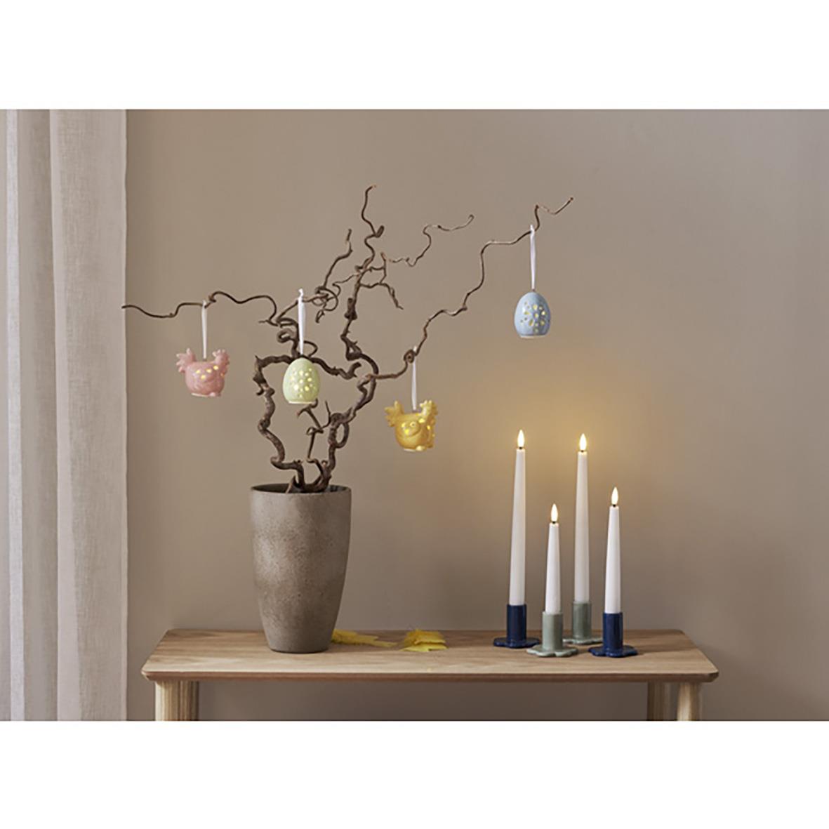 Dekorationsfigurer Esther med små äggformade dekorationer hängande från en gren i ett vaser på ett bord