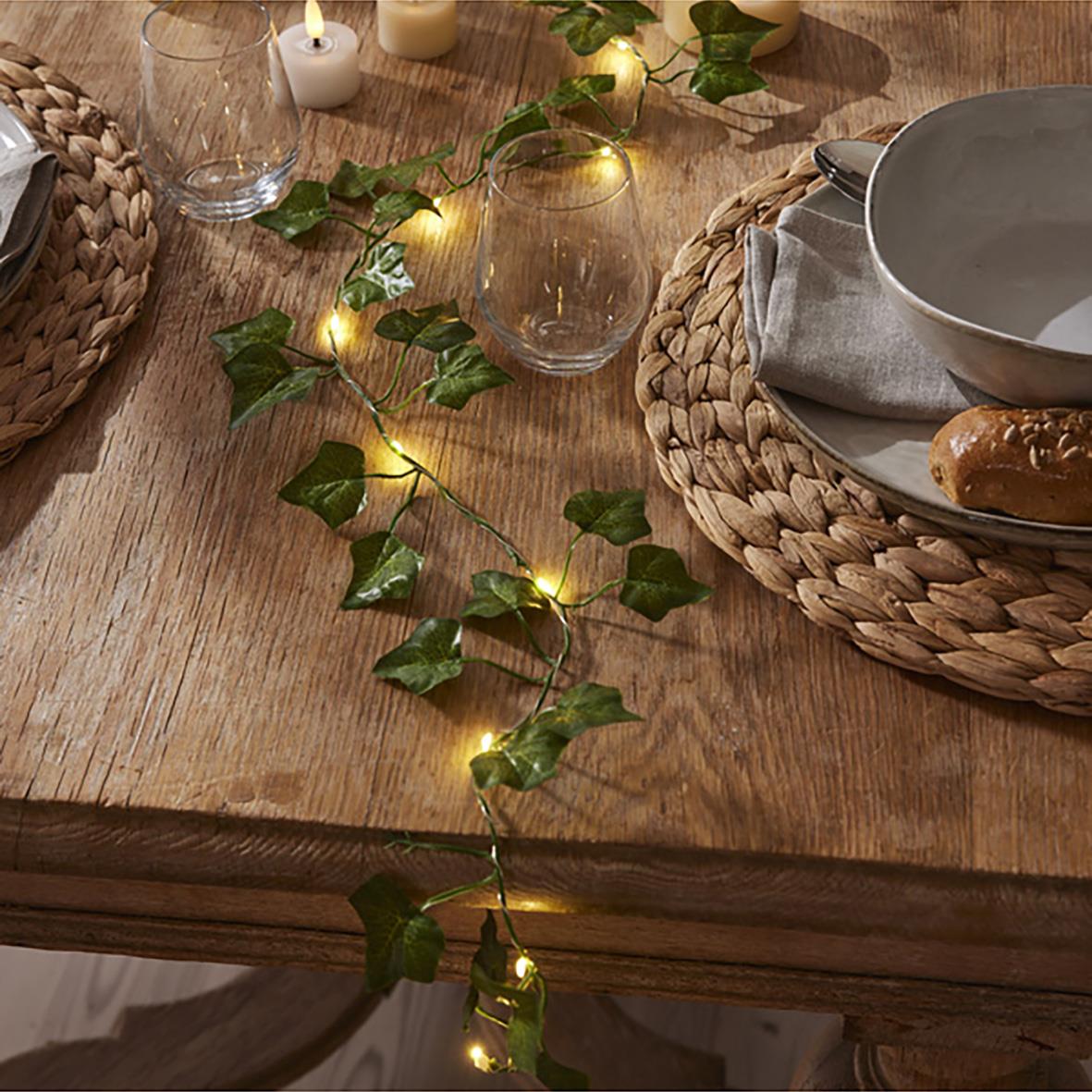 Ljusslinga Ivy med små varma ljus, dekorerad på ett träbord med glas, tallrikar och ljuslyktor