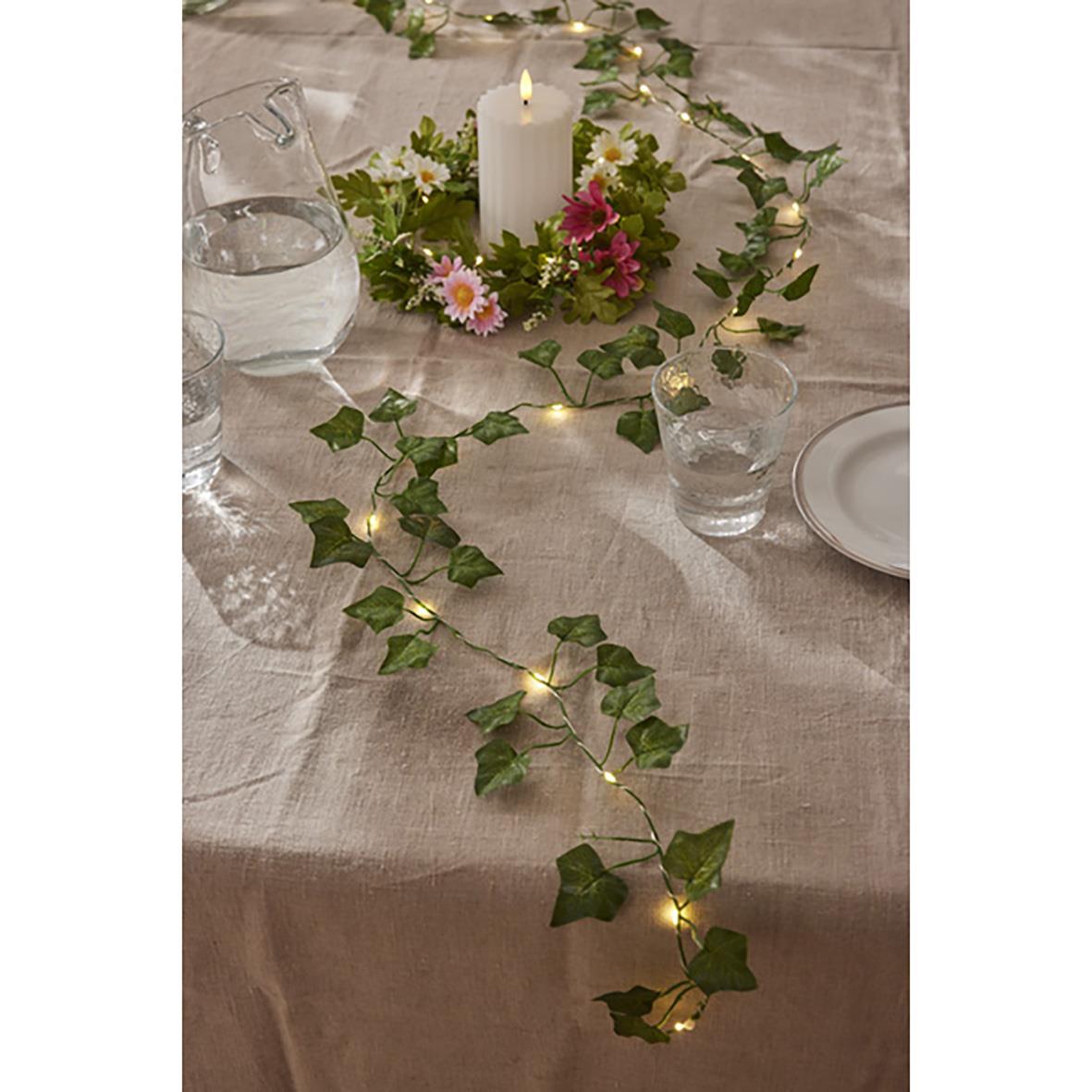 Ljusslinga med murgröna Ivy och små varma ljus på dukat bord med blomsterarrangemang och ljuslyktor
